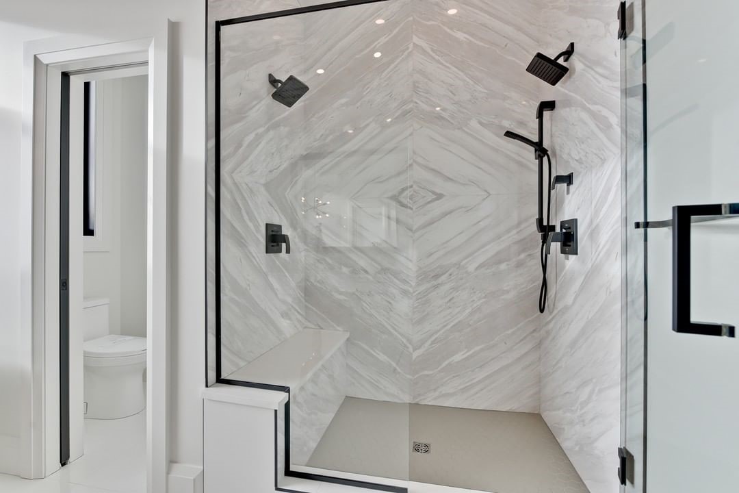 Spacious glass shower with chevron marble-look tile, bench, and dual shower fixtures