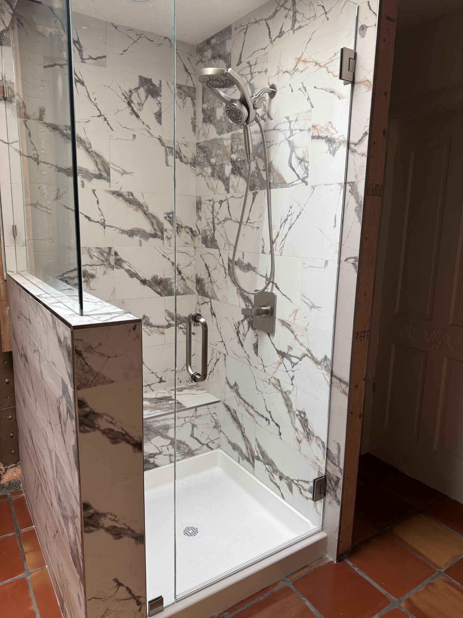 Completed custom shower with marble-look tile, half-wall, and frameless glass
