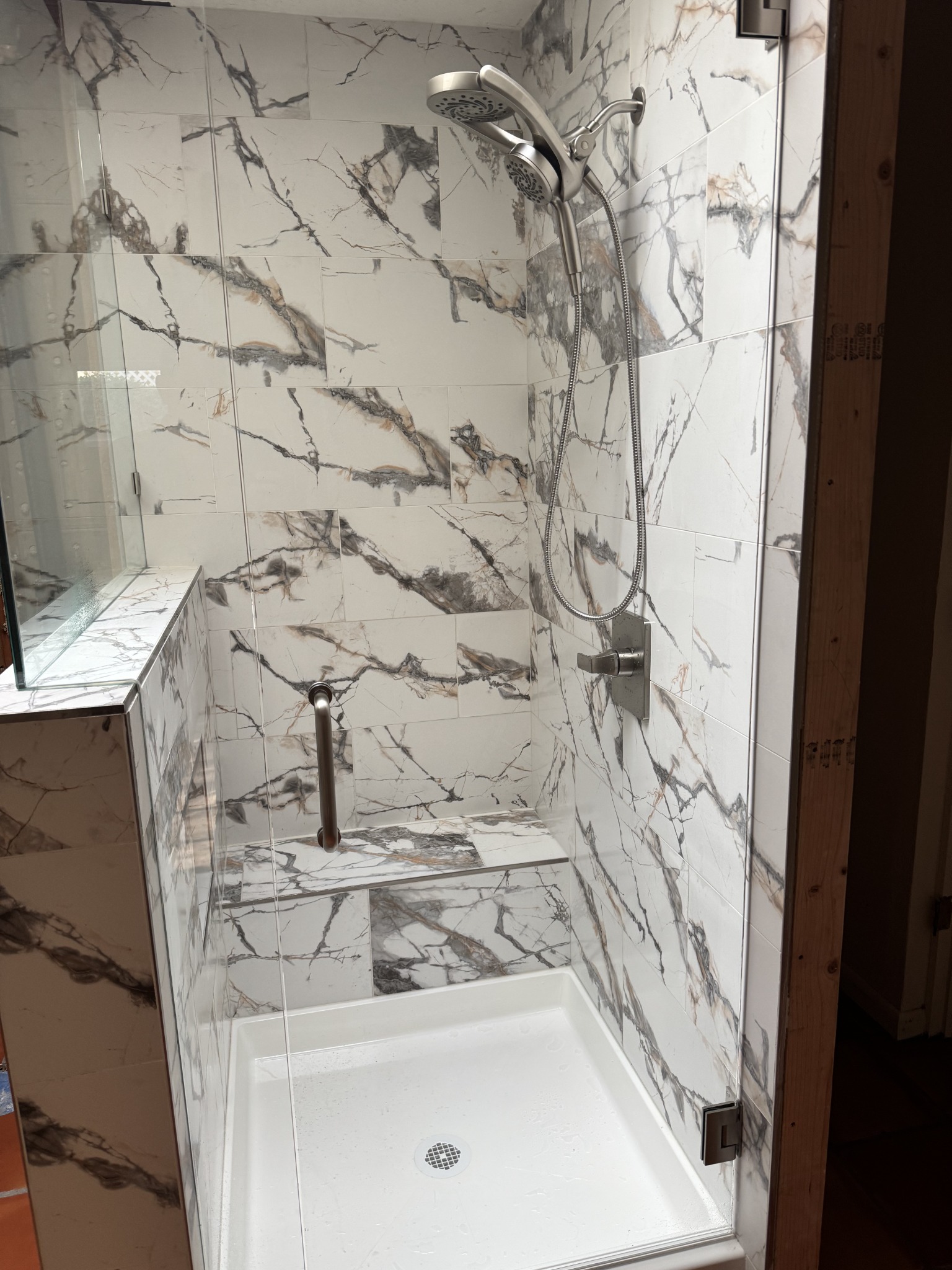 Completed marble-look tile shower with dual shower fixture and glass enclosure