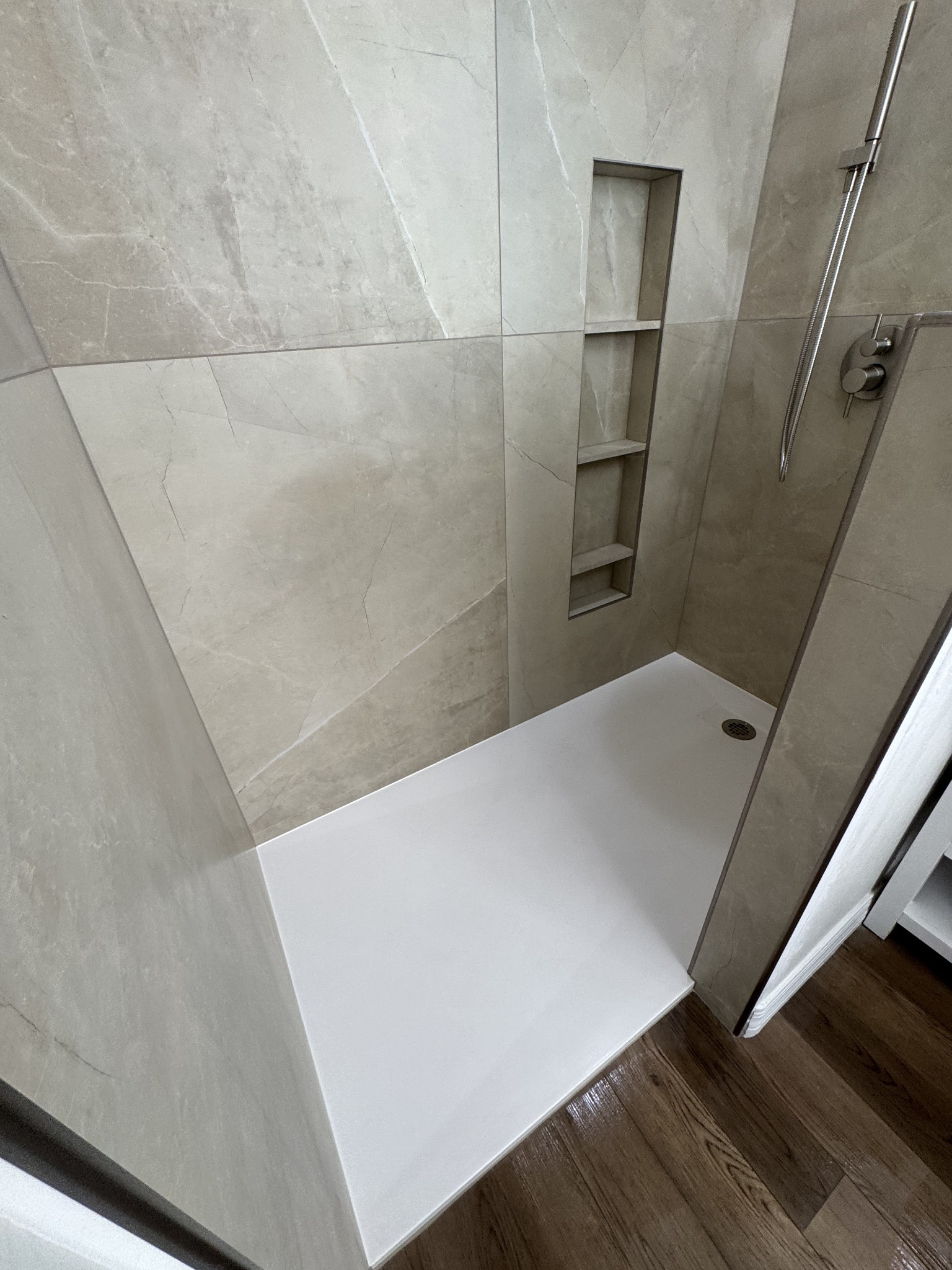 Completed walk-in shower with large-format tile, built-in niche, and handheld fixture